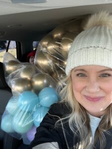 Image of Allyson Valentine in her Balloon Deliveryr van with son peeking through the balloons